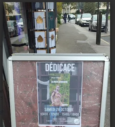 Affiche « Dédicace » sur le trottoir devant la librairie, montrant la couverture de La Piste africaine et la date du samedi 28 octobre